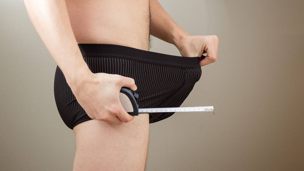 A man is measuring his penis with a measuring tape.