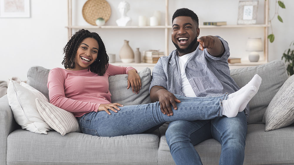 A couple sitting on a couch and pointing at something.