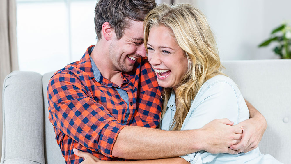 A man and woman hugging while sitting on a couch.